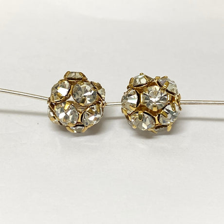 Pair of gold and crystal beads on a pin on a white background