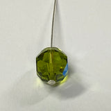 Green faceted crystal bead held by a pin on a white background