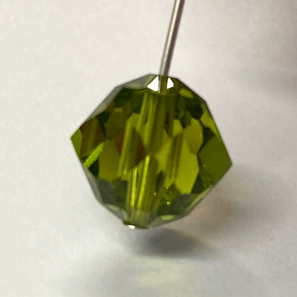 Green faceted crystal bead held by a pin on a white background