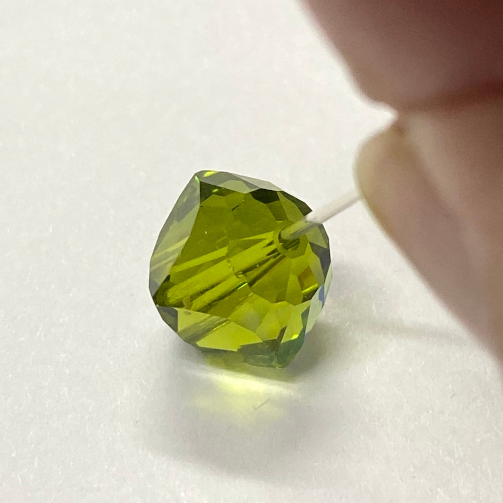 Green faceted crystal bead held by a hand on a white background