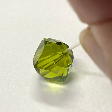 Green faceted crystal bead held by a hand on a white background