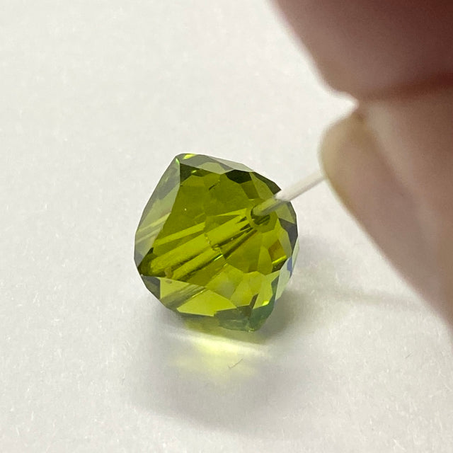 Green faceted crystal bead held by a hand on a white background