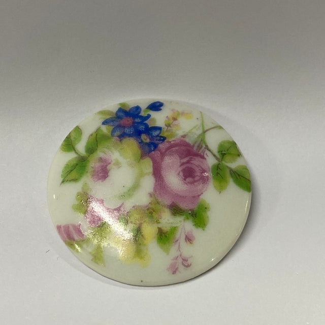 Floral design on a round ceramic item with purple roses and blue flowers.
