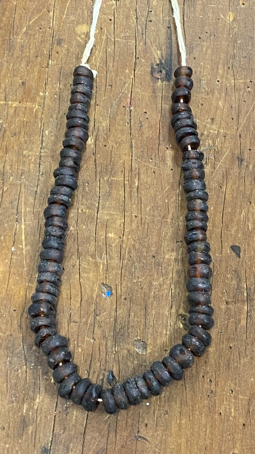 Strand of graded sized dark brown recycled glass beads on a wooden surface