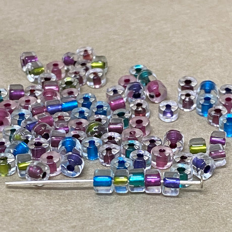 Assorted colorful beads on a beige surface including kiwi berry blue purple teal with some on a pin to show shae