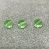 Three green vaseline glass vintage beads on a gray surface