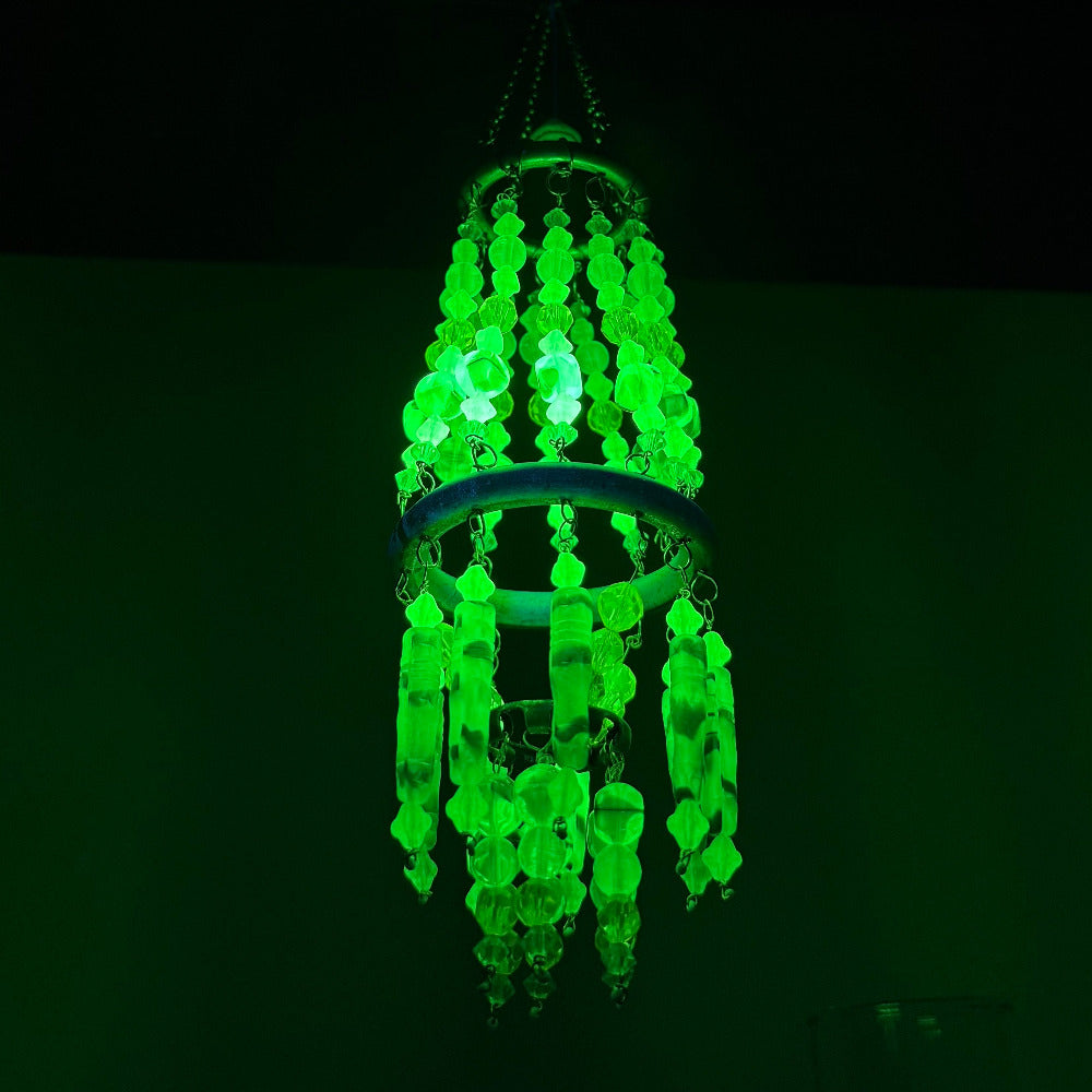 Decorative wind chime with vaseline uranium green and yellow beads hanging indoors under black light