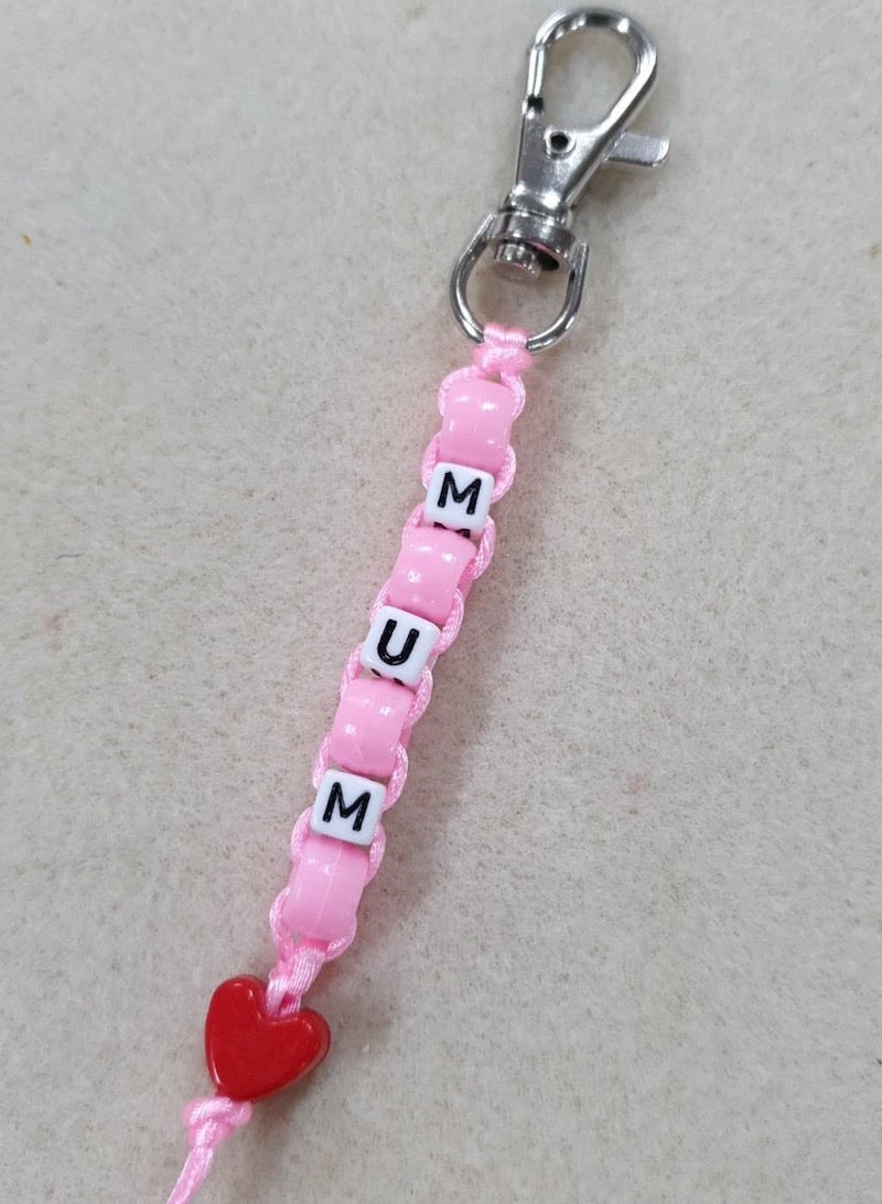 Pink beaded keychain with 'MUM' and a red heart charm on a light gray background