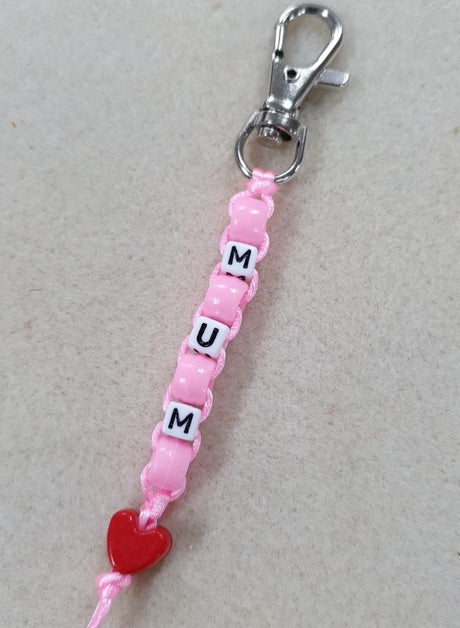 Pink beaded keychain with 'MUM' and a red heart charm on a light gray background