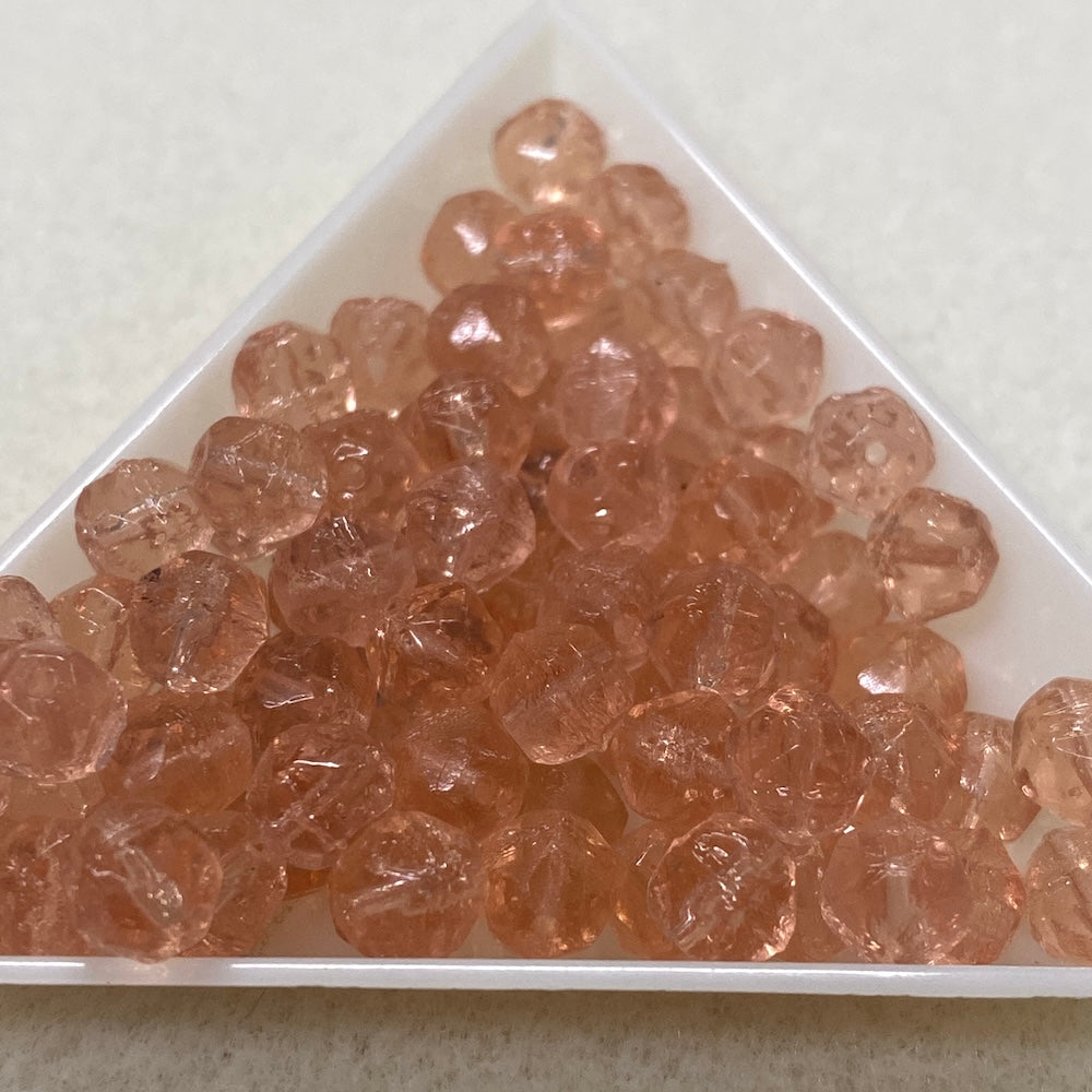 Clear pink glass beads in a triangular container on a light background