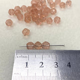 Small pink beads on a white background with a ruler for scale.