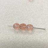 Three pink beads on a needle against a light gray background
