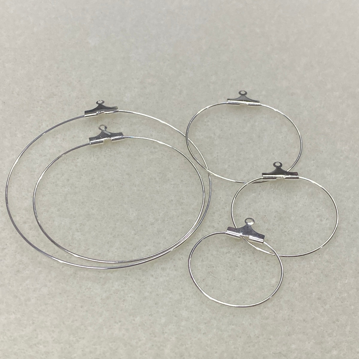 Set of five graded sized metal ear hoop earring fittings with clips on a gray background