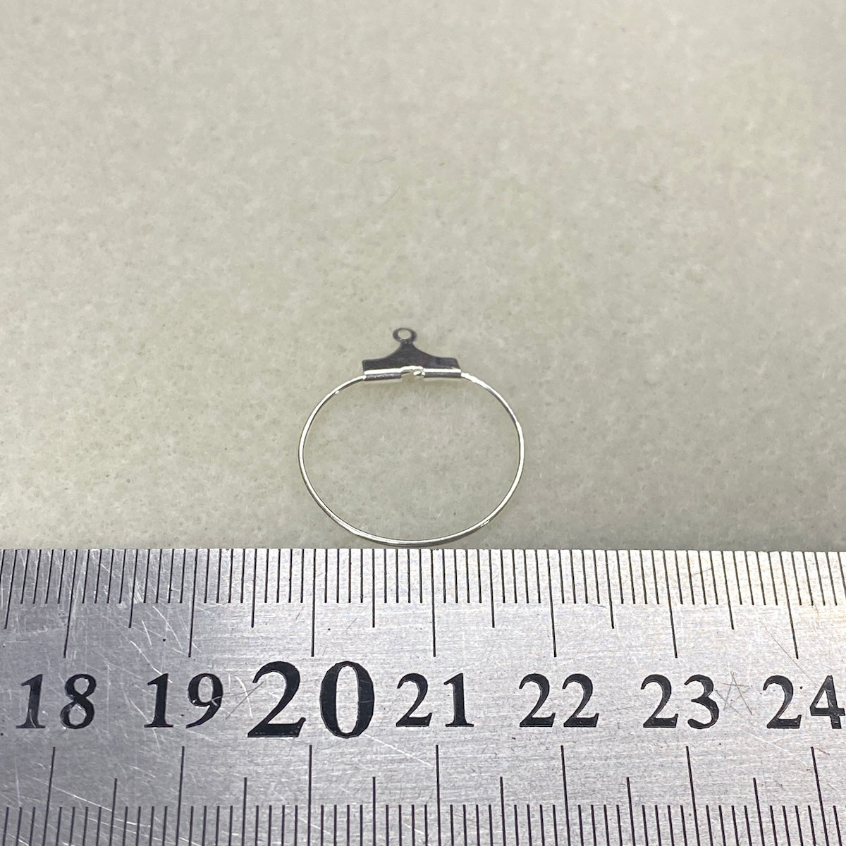 Silver hoop ear ring on a ruler for size measurement against a gray background