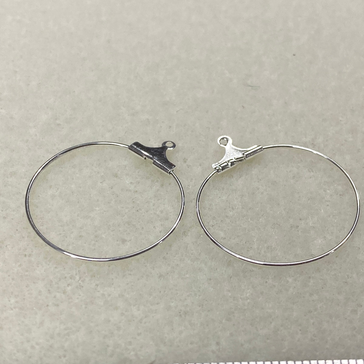 Two silver hoop earrings with clips on a light gray background