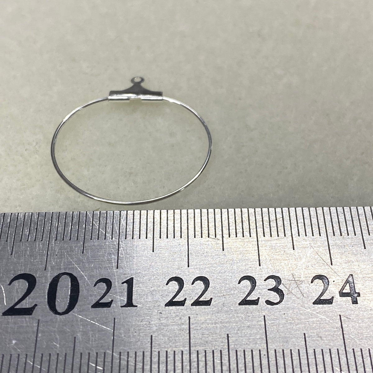 Silver hoop ear ring on a metal ruler with measurements