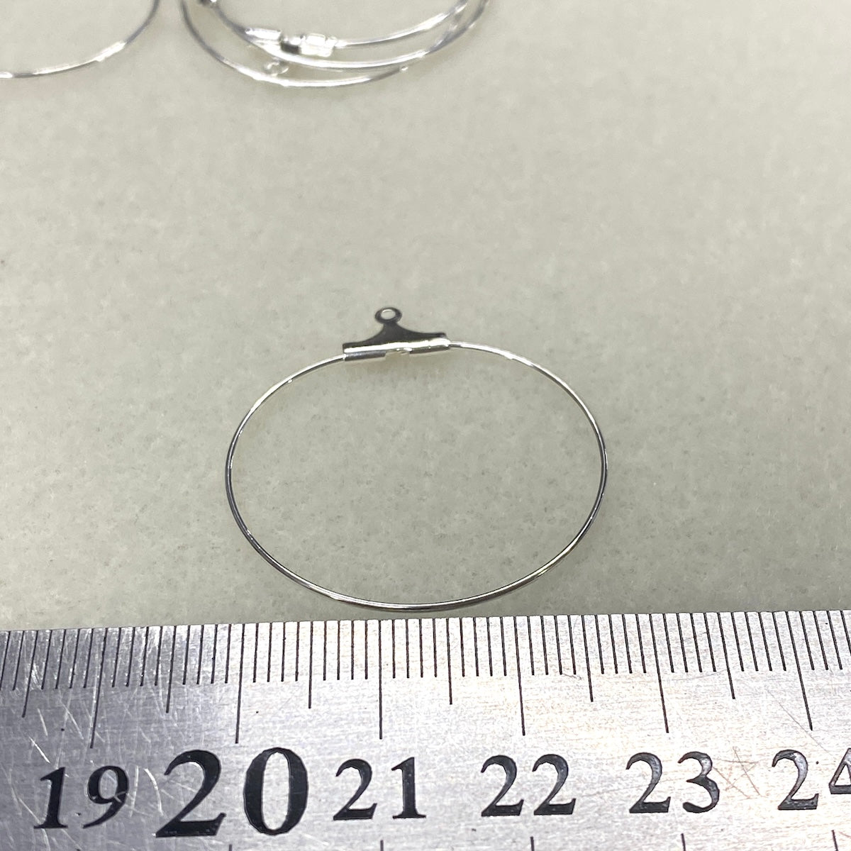 Silver hoop earring on a gray background with a ruler for scale.