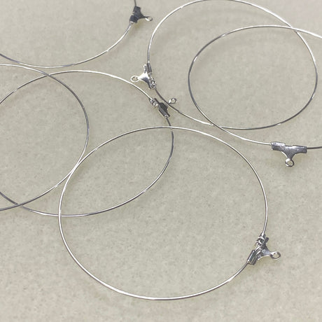Silver wire ear loop fittings with clasp ends on a beige background