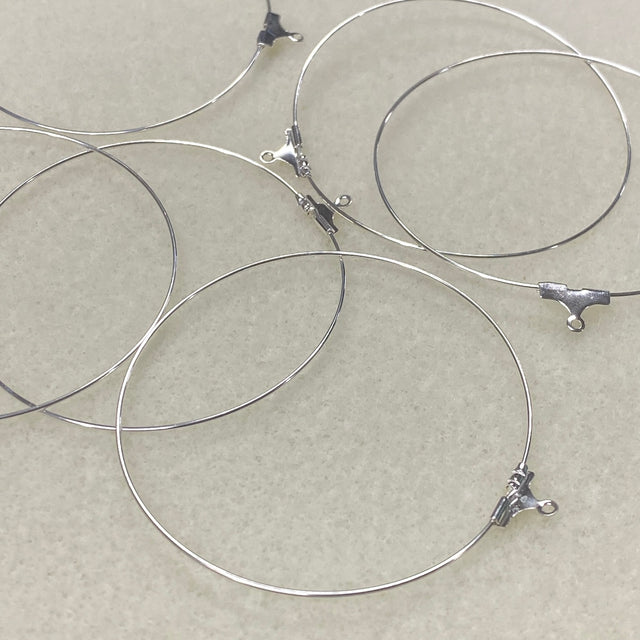 Silver wire ear loop fittings with clasp ends on a beige background