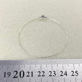 Silver ear hoop fitting on a light gray background with a ruler for scale.