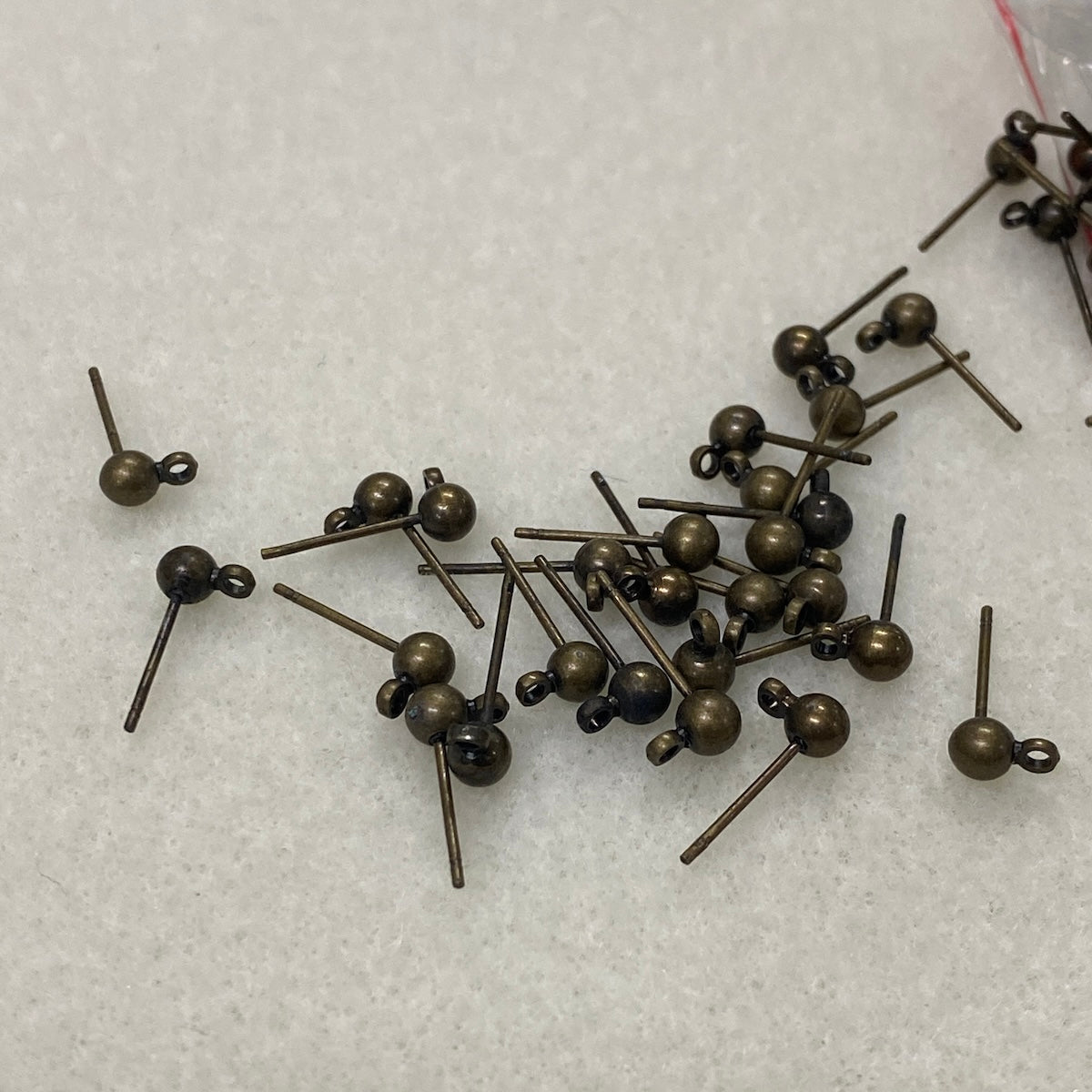 Bronze-colored ear stud fittings scattered on a white textured surface