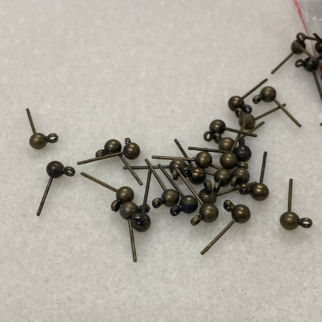 Bronze-colored ear stud fittings scattered on a white textured surface