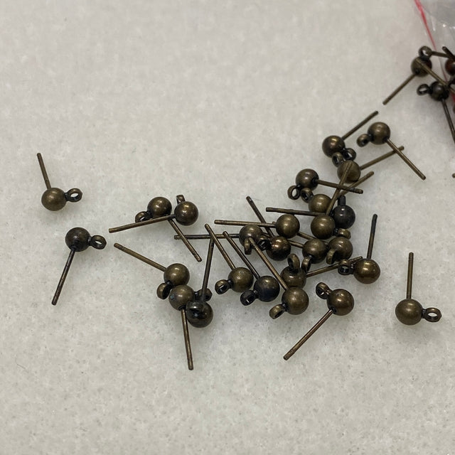 Bronze-colored ear stud fittings scattered on a white textured surface