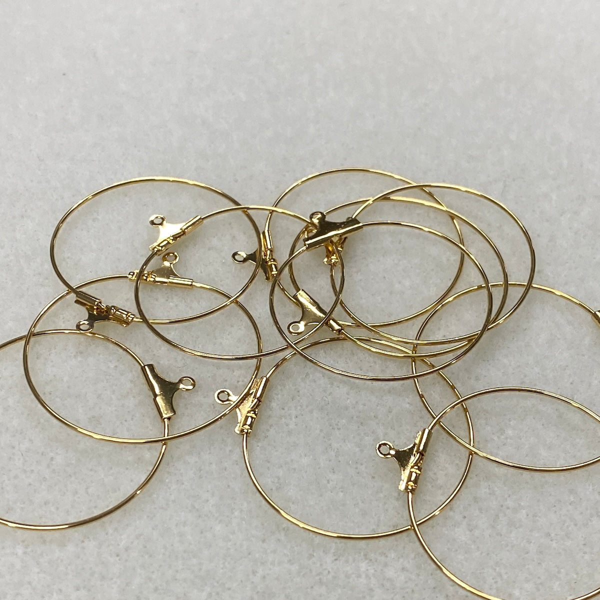 Gold hoop earrings with clasps on a light gray background