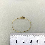 Gold circular metal frame with a small hook on top, next to a ruler for scale on a light gray background.
