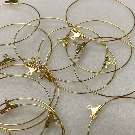 Gold hoop earrings with clasp mechanisms on a light gray background