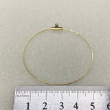 Gold circular ear hoop with a hook on a gray background, measured against a ruler.