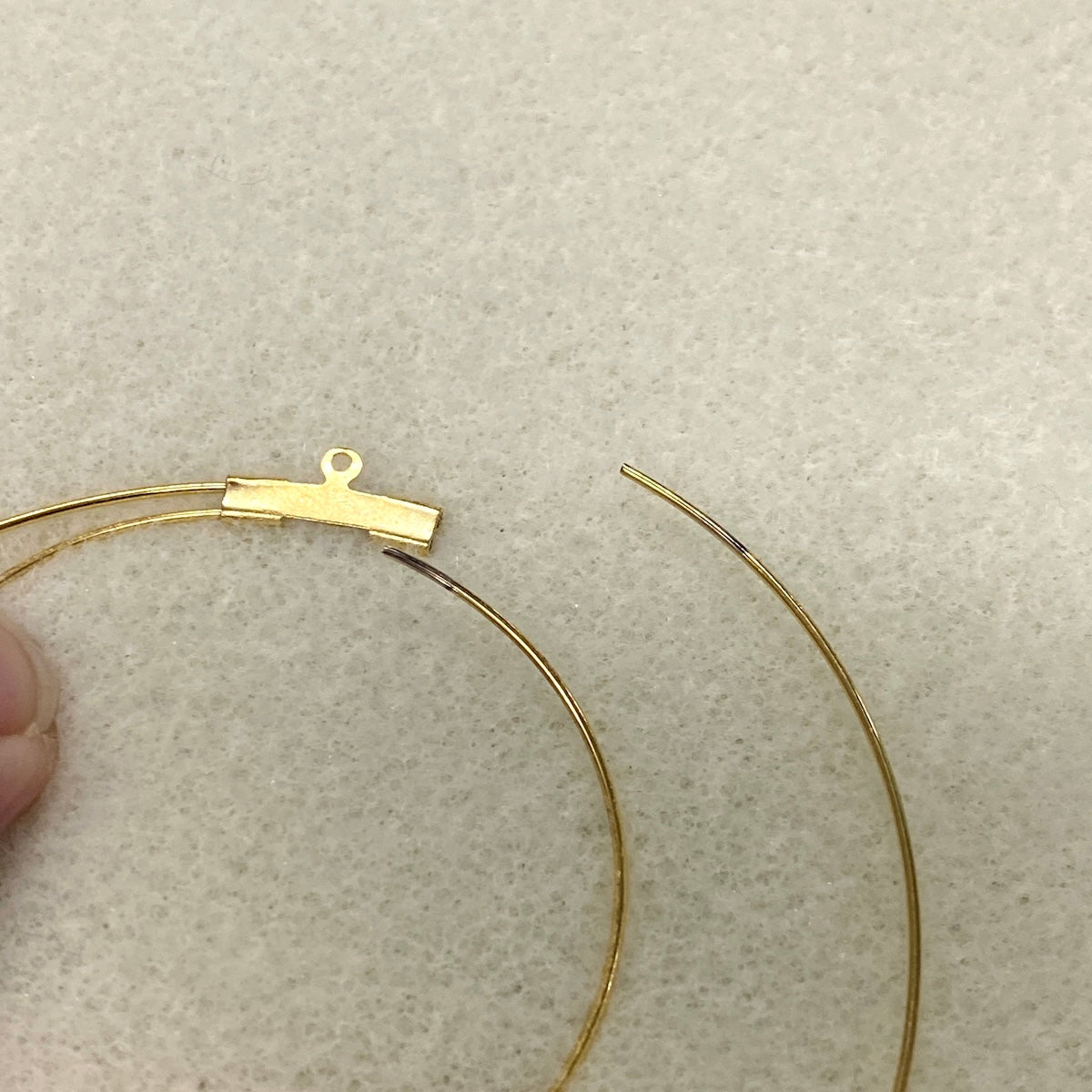 Gold double ear hoops on a textured beige surface