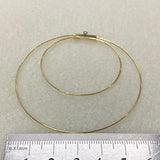Gold hoop earring on a light gray background with a ruler for scale.