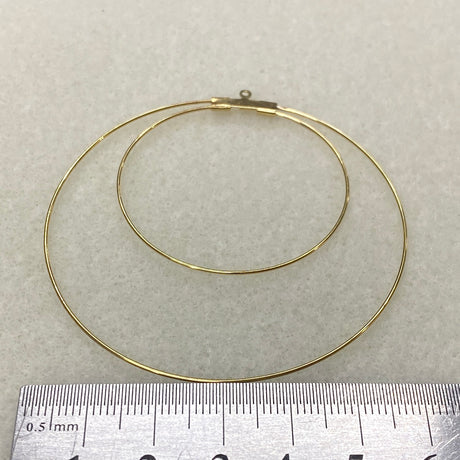 Gold hoop earring on a light gray background with a ruler for scale.