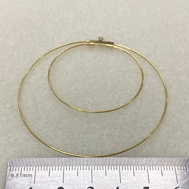 Gold hoop earring on a light gray background with a ruler for scale.