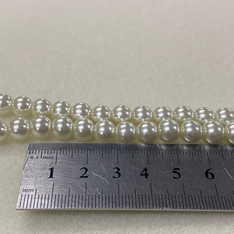 String of pearls with a ruler for size reference on a light gray background