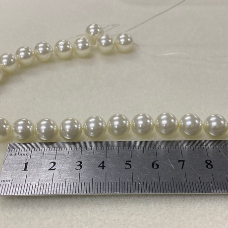 Pearl necklace with a ruler for scale on a light background