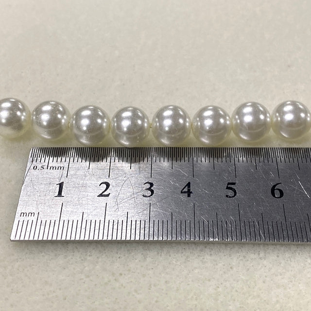 Row of pearls with a metal ruler for scale on a light background