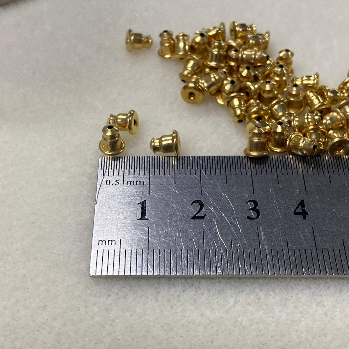 Gold bullet ear stud backs with a ruler for scale on a light gray background