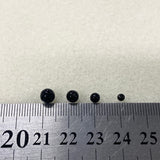 Four black beads on a ruler for size reference against a white background
