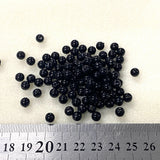 Black beads on a white background with a ruler for scale.