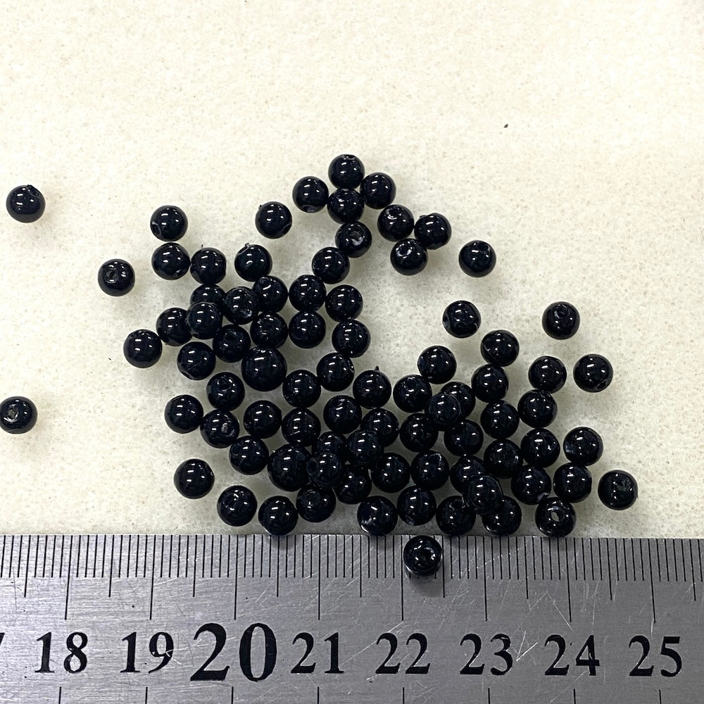 Black beads on a white background with a ruler for scale