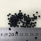 Black beads on a white background with a ruler for scale