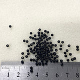 Small black beads on a white background with a ruler for scale.