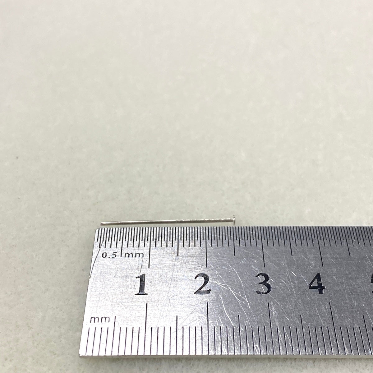 one headpin against Metal ruler on a textured beige surface