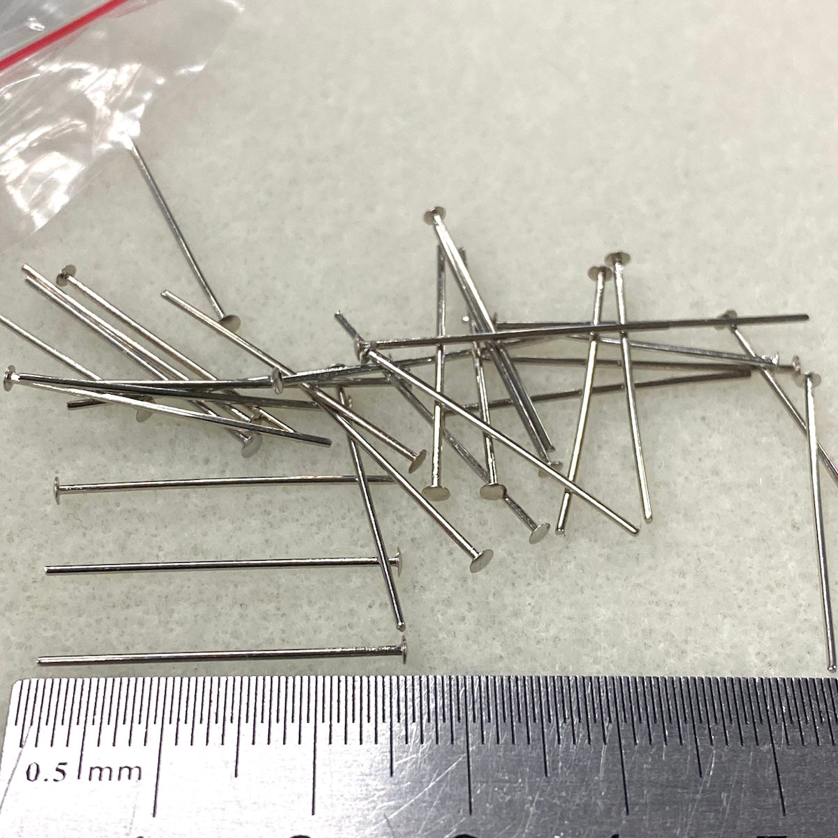 Metal pins with a ruler for scale on a textured surface