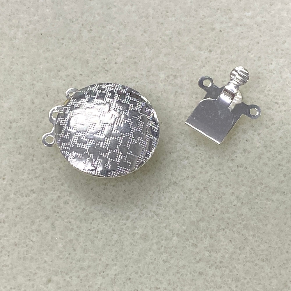 Two halves of a silver metal clasp on a beige background