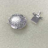 Two halves of a silver metal clasp on a beige background