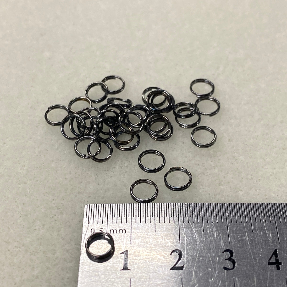 Small metal jump rings on a light gray background with a ruler for scale.