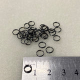 Small metal jump rings on a light gray background with a ruler for scale.